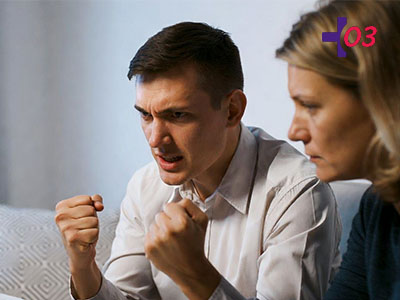 Мужчина сжимает кулаки и челюсти, рядом сидит женщина